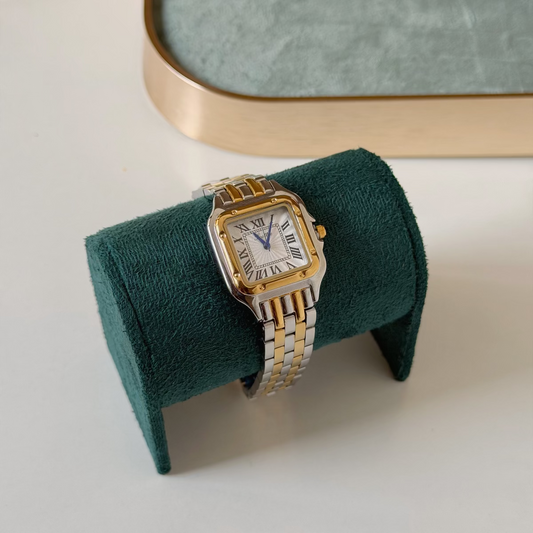 A two-tone metal wristwatch with a silver-toned case and bracelet, gold-toned accents, and a white dial, displayed on a dark green velvet stand.