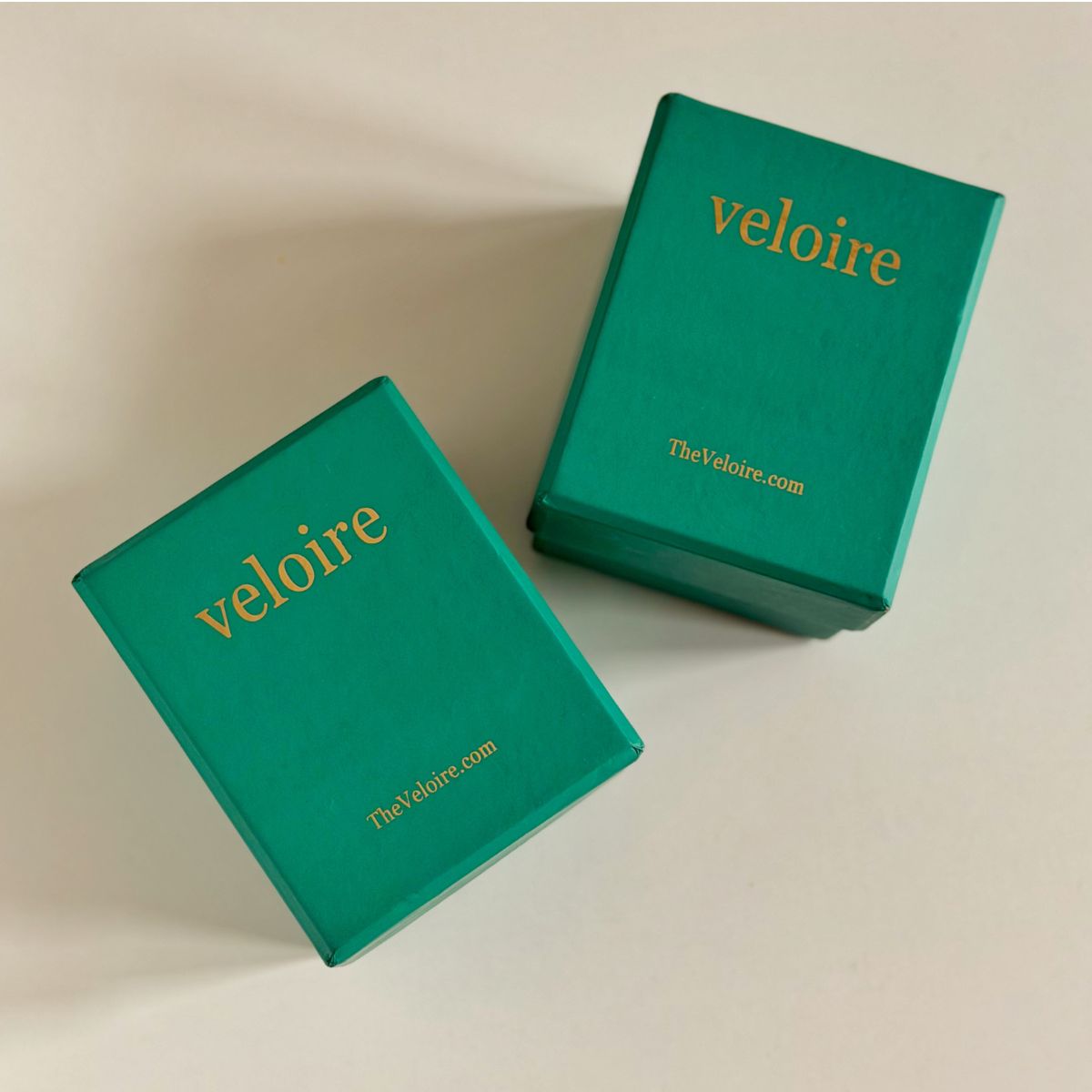 Two teal green velvet jewelry boxes with gold foil 'veloire' branding, displayed on a light beige background.