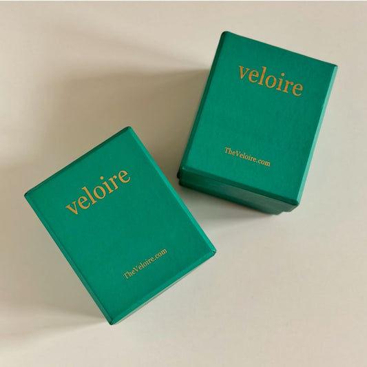 Two teal green velvet jewelry boxes with gold foil 'veloire' branding, displayed on a light beige background.