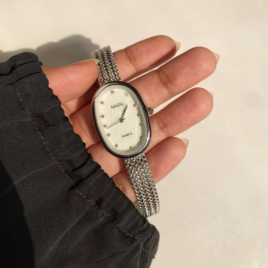A silver-tone mesh-strand watch with an oval white dial and crystal, held in a person's hand. The brand name 'RADI' is visible on the dial.